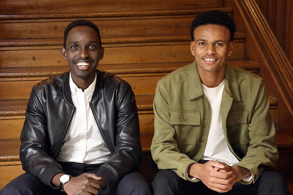 Two men pose for a photo together sitting on wood steps.